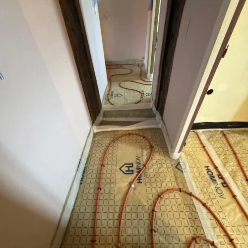 Continuité des tuyaux de plancher chauffant à travers un passage de porte et bande périphérique résiliente